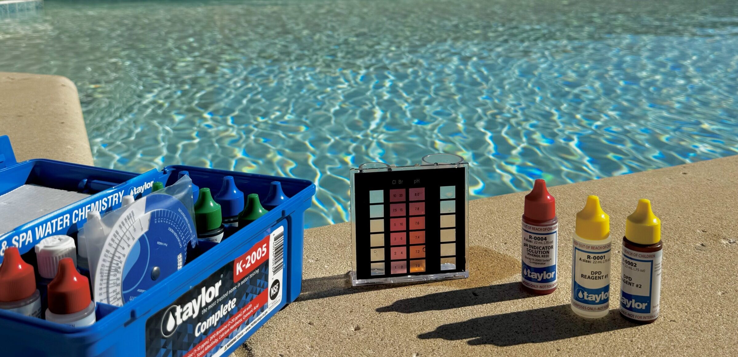 Poolside scene with a water testing kit, including various bottles and a color chart, set near a shimmering swimming pool.