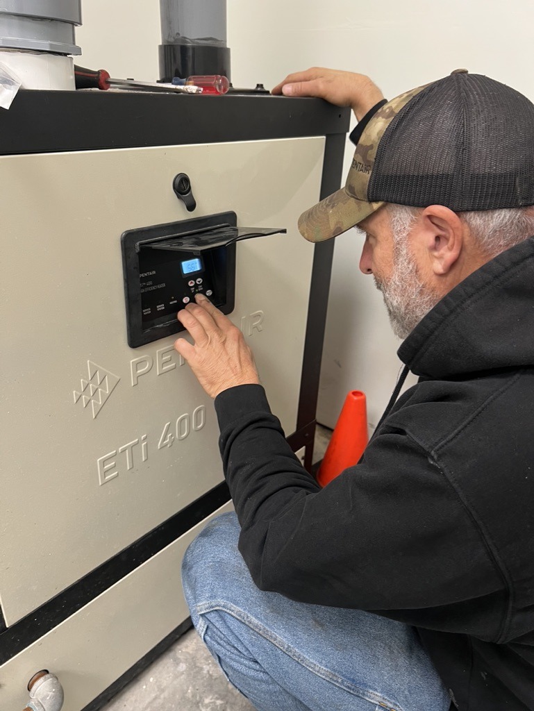 A person adjusts controls on a Pentair ETi 400 machine, wearing a cap and hoodie. An orange cone is visible beside them.