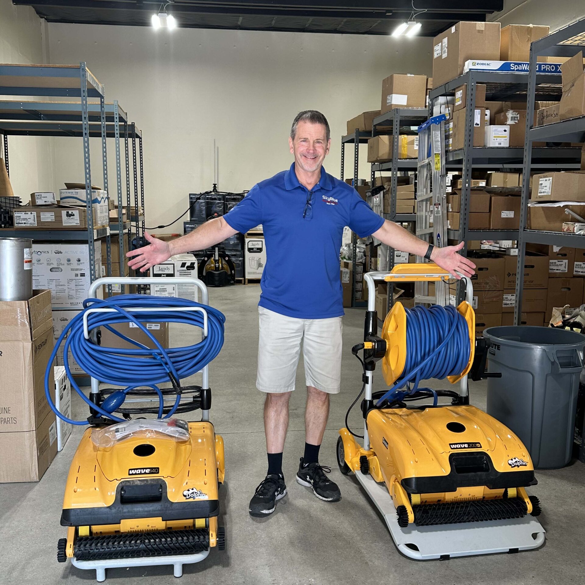 A person in a warehouse with cleaning equipment smiles, surrounded by boxes and shelves. Industrial setting with commercial products visible.