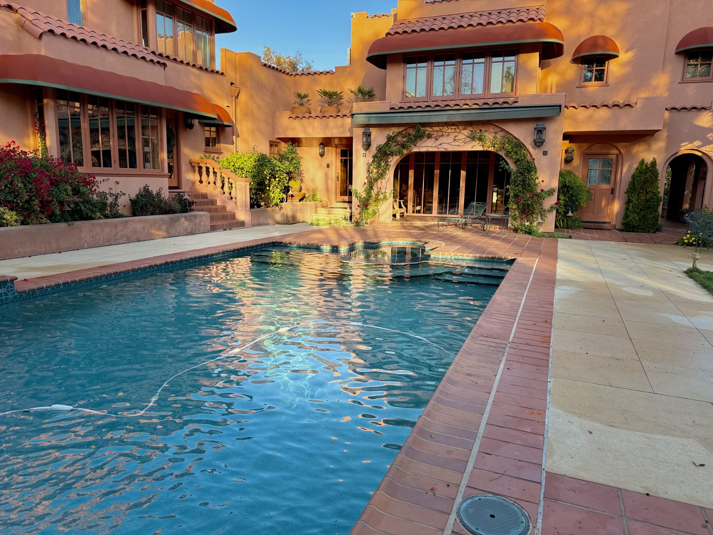 A Mediterranean-style villa features a serene swimming pool, surrounded by lush greenery and warm-toned architecture, basking in the afternoon sun.