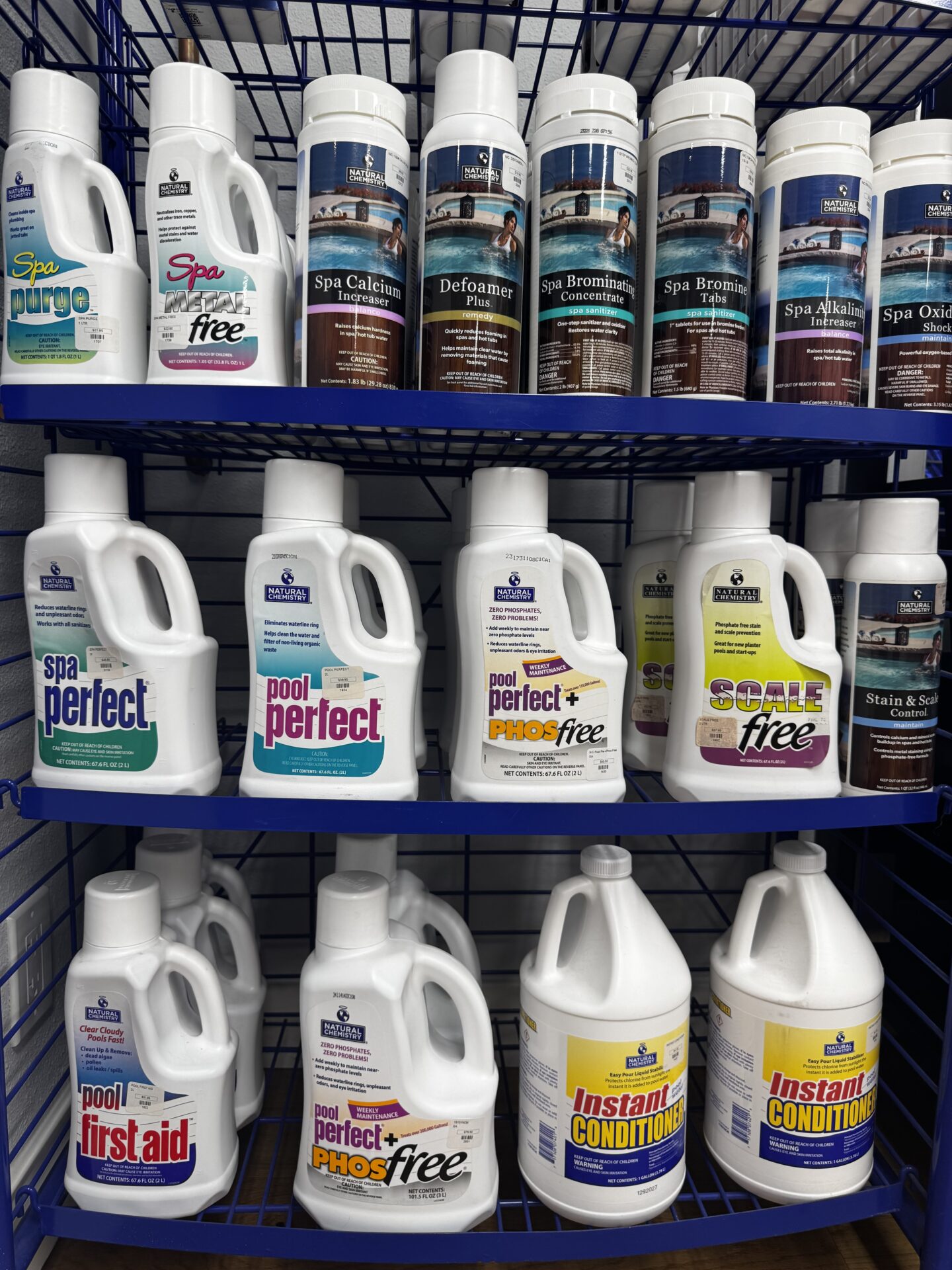 Shelves displaying various spa and pool care products in plastic bottles, organized by type, including treatments for algae, bromine, calcium, and cleaning solutions.