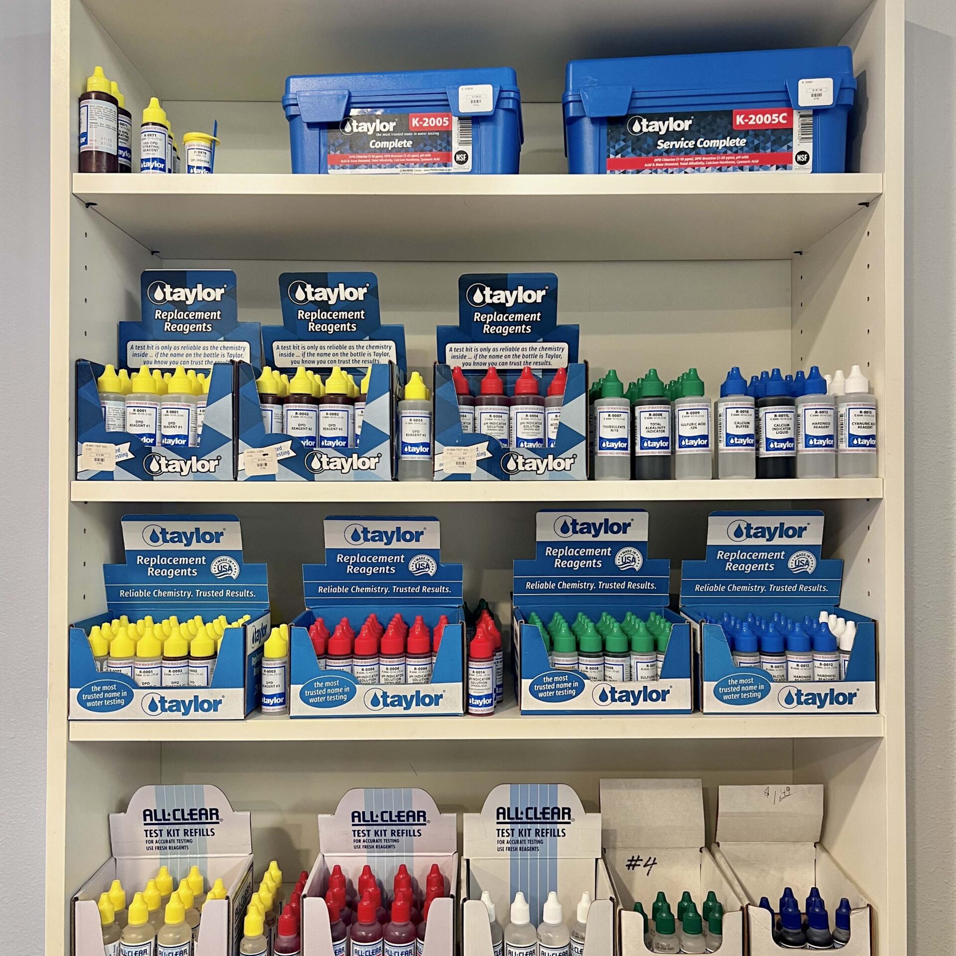 Shelves are filled with various Taylor pool testing reagents and supplies in colorful bottles, neatly organized, likely in a store or testing facility.