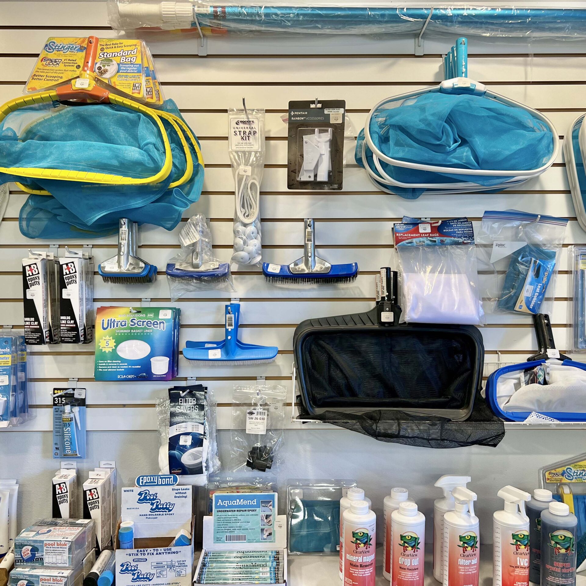 A store display featuring various pool supplies including nets, brushes, cleaning solutions, and accessories arranged neatly on a wall with price tags.