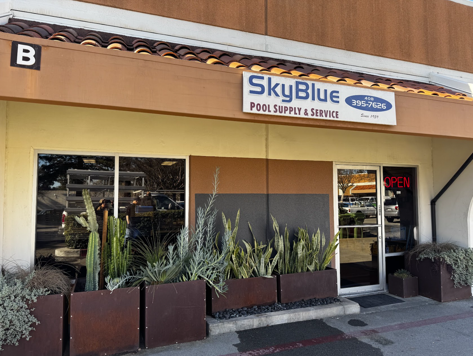 A storefront for "SkyBlue Pool Supply & Service" with plants outside. There's an "OPEN" sign on the door and a contact number displayed.